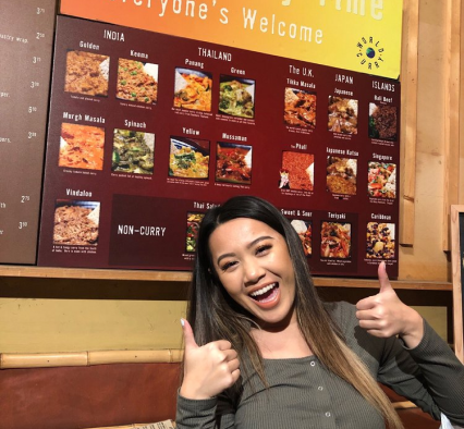 A girl with two thumbs up in front of our menu board